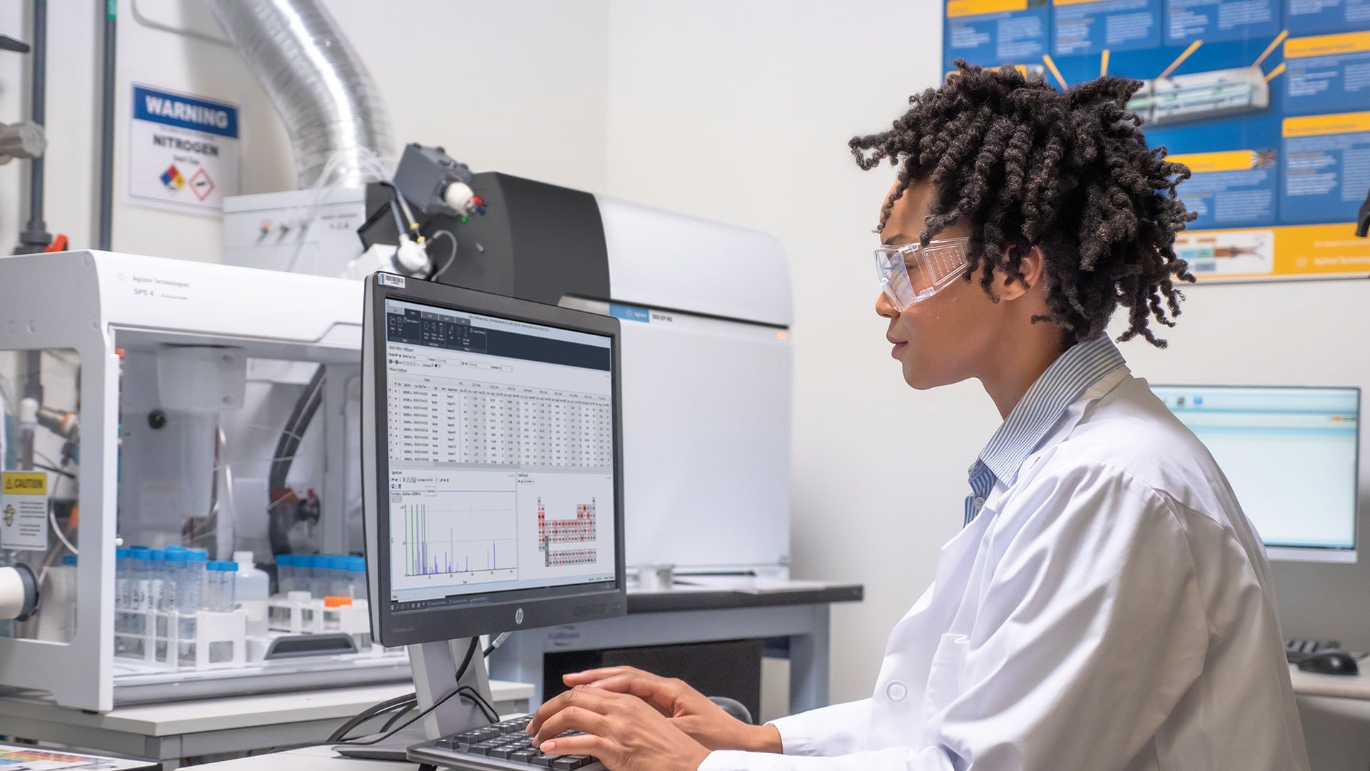 A scientist in a lab coat and goggles works intently on a computer, analyzing data. The lab is equipped with advanced scientific equipment, conveying focus and precision.