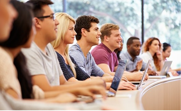 People seated in a classroom using laptops during a presentation.