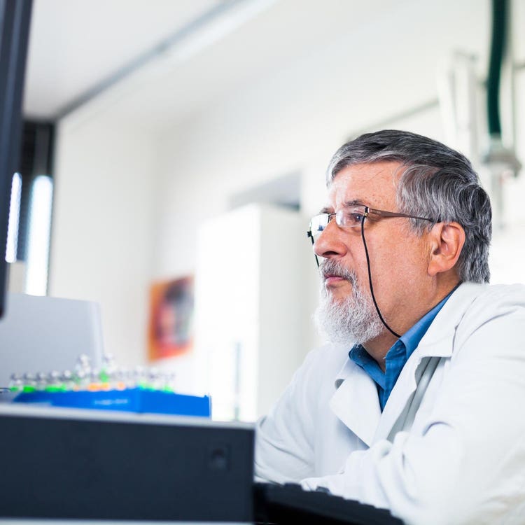 Scientist in a lab coat working at a computer beside laboratory equipment.